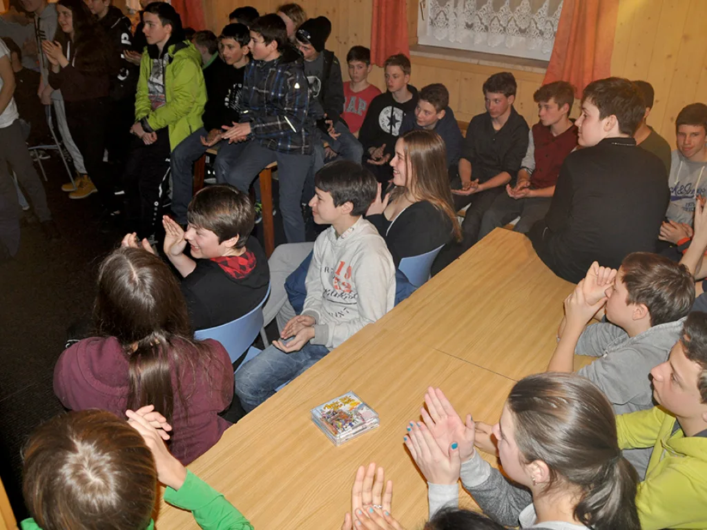 Jugendliche sitzen abends an Tischen und applaudieren.